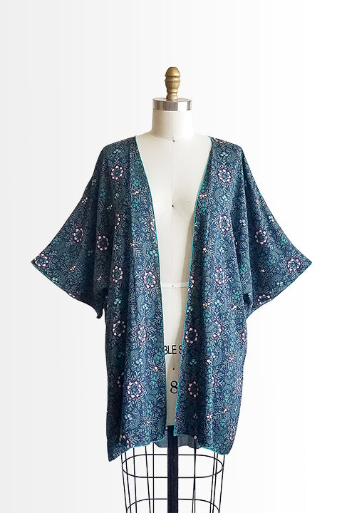 front view of small batch open front fashion kimono made from a 100% rayon midnight blue fabric printed with fireflies and a pink and green floral motif shown on a dress form