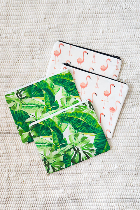 image of 4 classic zip pouches laying on an off white rag rug.  There are 2 zip pouches made from a green, tropical leaves cotton print and 2 bags that are made from a pink flamingos cotton print.