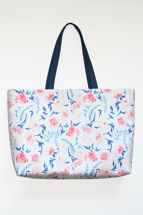 image of a large oversize tote bag made out of cotton canvas. the handles are a dark blue canvas and the body of the tote is a white fabric printed with light pink and blue watercolor flowers