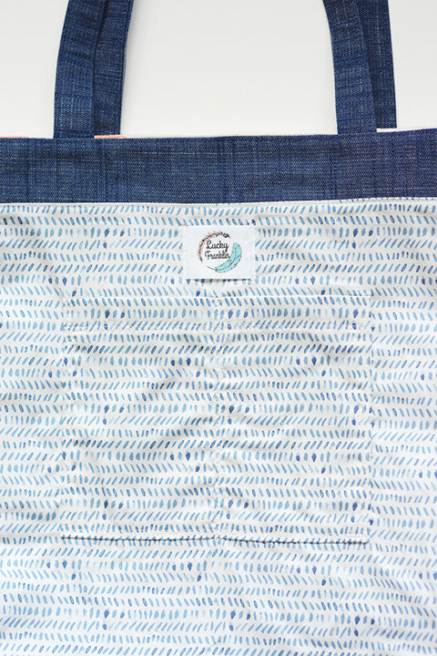 a detailed view of the lined interior of the tote bag. the lining is a print with light blue watercolor dashes on a white background. the interior shows the old lucky franklin label and 2 interior pouch pockets.