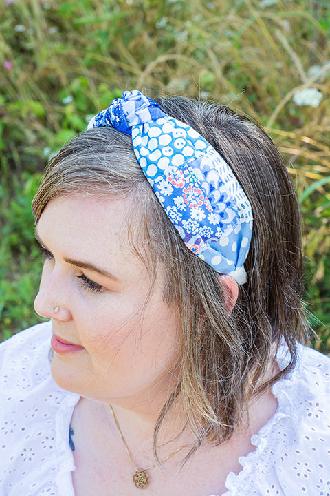 image of a female model wearing a one-of-a-kind top knot headband.  The headband is made from patchworked and quilted fabric scraps in a collection of blue floral and geometric prints.