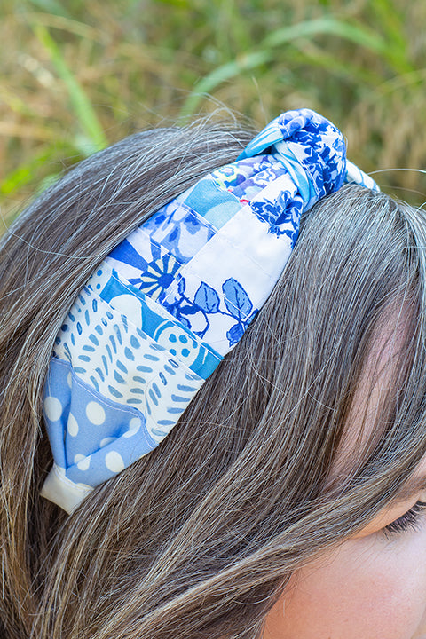 image of a female model wearing a one-of-a-kind top knot headband.  The headband is made from patchworked and quilted fabric scraps in a collection of blue floral and geometric prints.