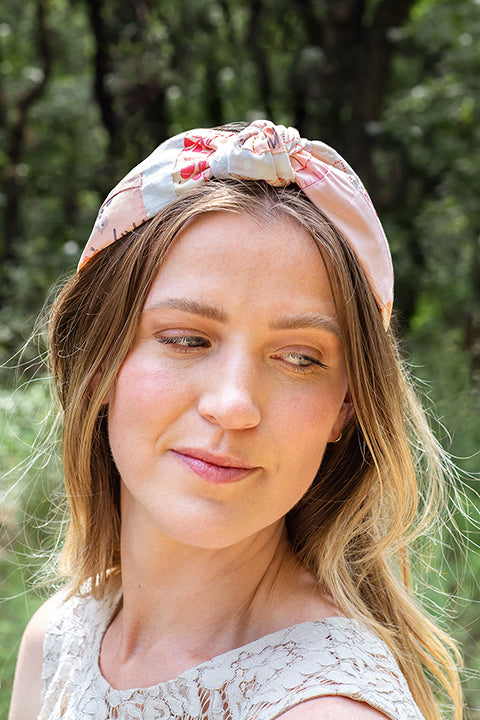 image of a female model wearing a one-of-a-kind zero-waste top knot headband.  The material on the headband is patchworked cotton scraps in a variety of pink floral and geometric prints.