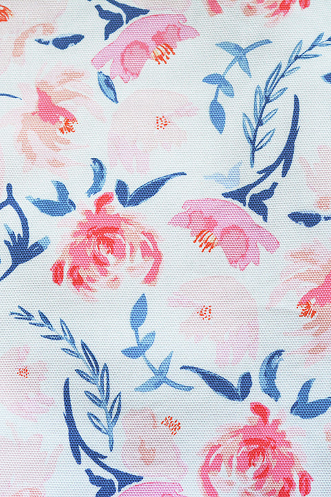 a view of the pretty canvas material that has a white background printed with light pink watercolor flowers and painterly light blue steams and leaves. you can also see the basketweave texture of the textile.