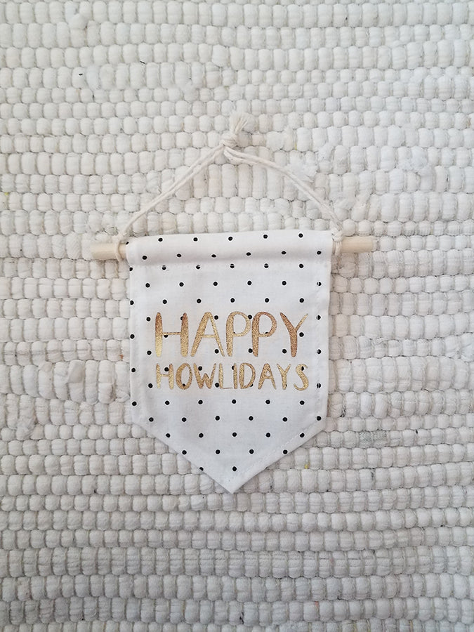 mini handmade pennant ornament featuring white with black dots fabric printed with gold words saying happy howlidays