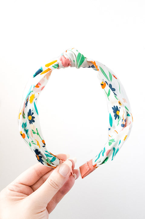 front view of an upcycled cotton fabric headband featuring a top knot and rainbow colored on white bright floral print fabric