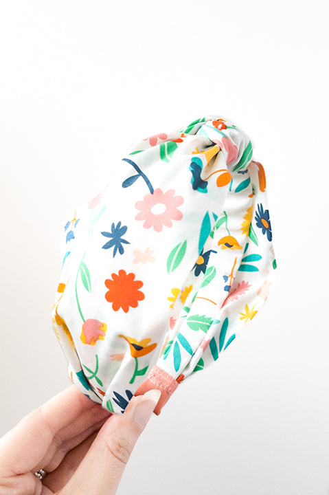 side view of an upcycled cotton fabric headband featuring a top knot and rainbow colored on white bright floral print fabric