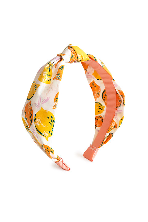image of a top knot style handmade headband in front of a white background. this headband was sustainably made using upcycled cotton material in a lemon themed print featuring orange and yellow fruit.