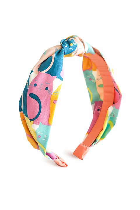 image of a top knot style headband shown in front of a white background. the headband is sustainably handmade from cotton fabric scraps in a color cat themed print.  the colors in the cat print are magenta, teal, aqua, yellow and orange.