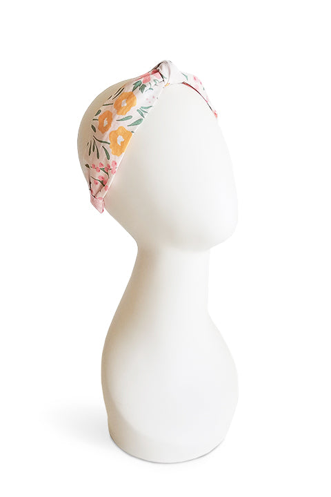 image of an upcycled handmade headband sustainably made from a 100% cotton fabric scraps in a happy floral print with cream, mustard yellow, green and pink, shown on a white colored display head in front of a white background