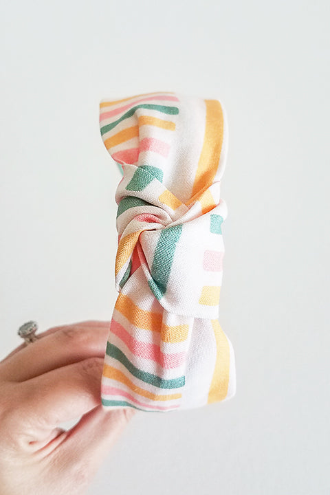 top knot view upcycled handmade headband made from a 100% cotton fabric scraps in a happy stripes geometric print with cream, mustard yellow, green and pink
