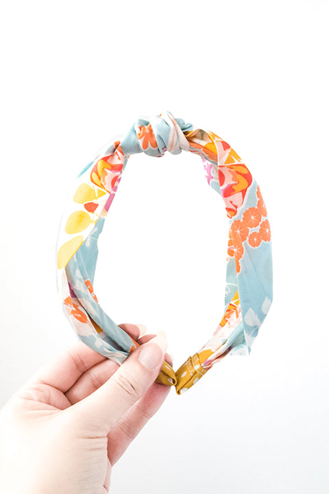 front view of an upcycled cotton fabric headband featuring a top knot and vibrant aqua, orange and pink colorful mosaic floral print fabric