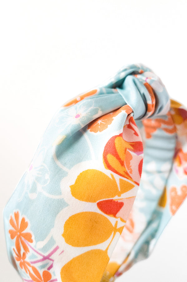 side detail view of an upcycled cotton fabric headband featuring a top knot and vibrant aqua, orange and pink colorful mosaic floral print fabric