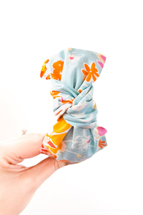 top view of an upcycled cotton fabric headband featuring a top knot and vibrant aqua, orange and pink colorful mosaic floral print fabric