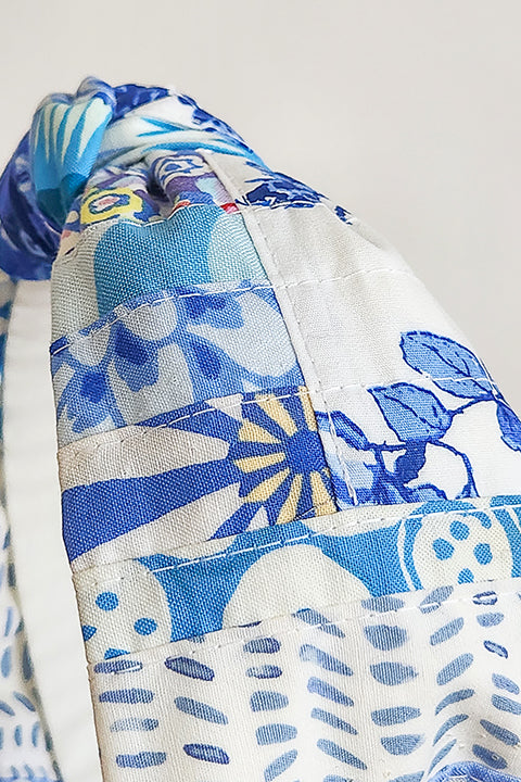 a close up, very zoomed in image of the patchwork and topstitching on a handmade and sustainable top knot style headband in front of a white background.  The cotton material on the headband is a unique patchworked textile created from scrap fabrics in shades of blue with white.  The prints feature florals, dots, geometric shapes and buttons.