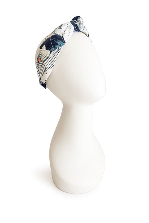 image of a hand stitched top knot style fabric headband on a white display head in front of a white background.  The material on the headband is a one-of-a-kind textile created from patchworking cotton scrap fabric.  The prints are in a black and white color palette with florals, checks, stripes, dots and triangles