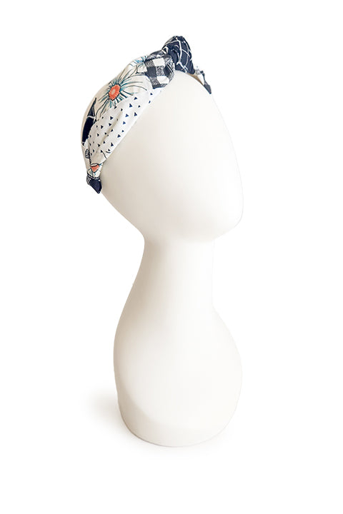 image of a handmade top knot style fabric headband on a white display head in front of a white background.  The material on the headband is a one-of-a-kind textile created from patchworking cotton scrap fabric.  The prints are in a black and white color palette with florals, checks, stripes, dots and triangles