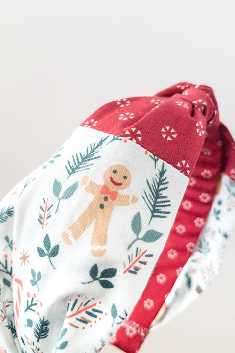 side detail view of an upcycled cotton fabric headband featuring a top knot and color-blocked prints, one with candy canes and gingerbread and the other a red petite peppermint print
