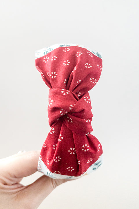 top view of an upcycled cotton fabric headband featuring a top knot and color-blocked prints, one with candy canes and gingerbread and the other a red petite peppermint print