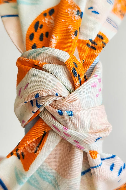 a zoomed in detailed view of the twisted top knot on a top knot style handmade headband in front of a white background. this headband was sustainably made using upcycled cotton material in a lemon themed print featuring pink and orange fruit with light blue accents..