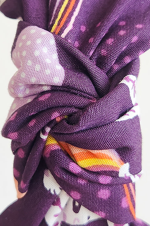 a zoomed in detailed view of the twisted top knot on a top knot styled handmade headband in front of a white background. Sustainably made from 100% cotton fabric scraps the print features boho white jaguars and yellow, pink and coral rainbows on a dark purple background.