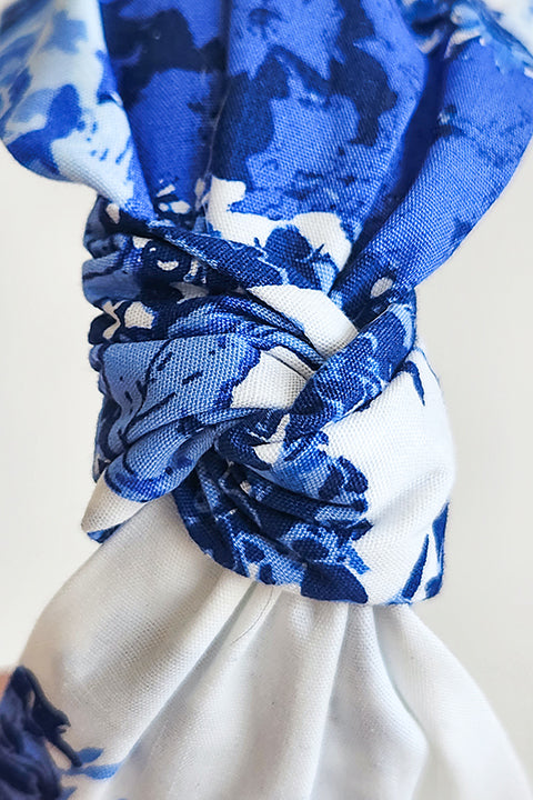 zoomed in close up image of a handmade top knot style headband in front of a white background. The headband is made from upcycled 100% cotton fabric scraps in a blue floral rose print on a white background.