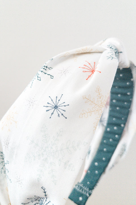 side  detail view of an upcycled cotton fabric headband featuring a top knot and white holiday snowflake print fabric
