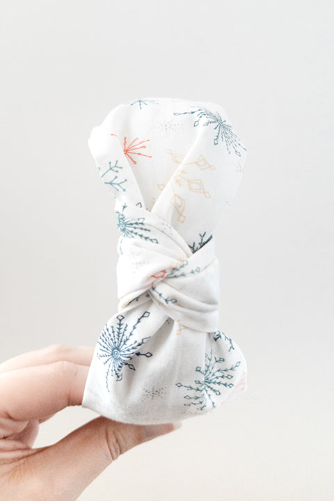 top view of an upcycled cotton fabric headband featuring a top knot and white holiday snowflake print fabric