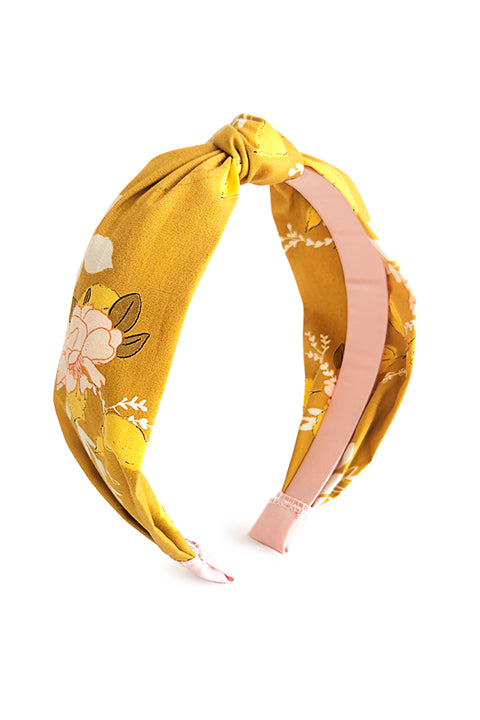 image of a top knot style sustainable handmade headband in front of a white background.  The 100% cotton material was upcycled from scraps and features a springy floral print in blush pinks on a mustard yellow background.