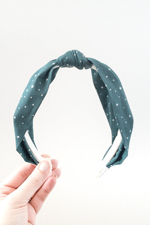 front view of an upcycled cotton fabric headband featuring a top knot and forest green holiday starry night print fabric