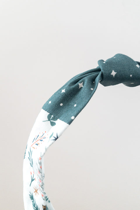 front detail view of an upcycled cotton fabric headband featuring a top knot and color-blocked prints, one with candy canes and gingerbread and the other a green starry night print