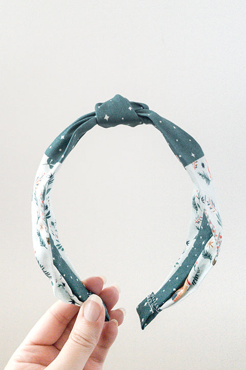 front view of an upcycled cotton fabric headband featuring a top knot and color-blocked prints, one with candy canes and gingerbread and the other a green starry night print