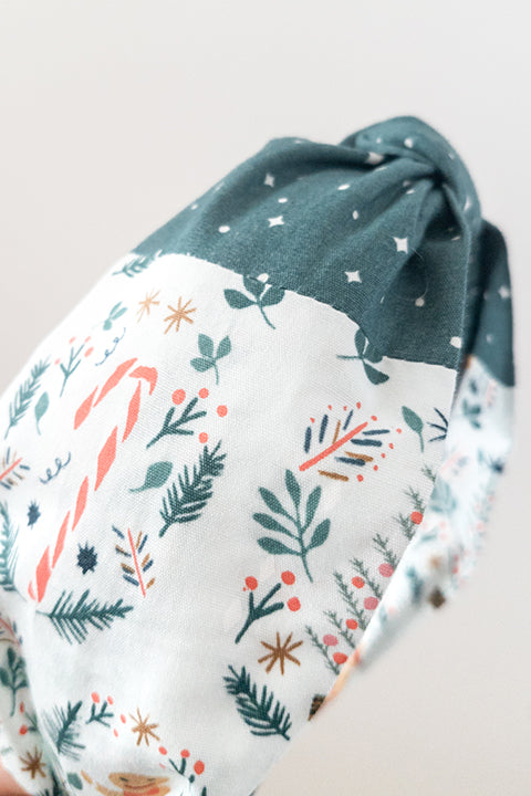 side detail view of an upcycled cotton fabric headband featuring a top knot and color-blocked prints, one with candy canes and gingerbread and the other a green starry night print