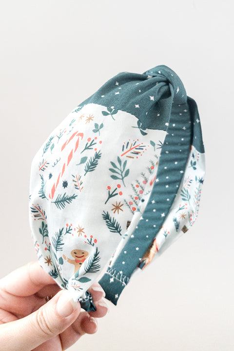 side view of an upcycled cotton fabric headband featuring a top knot and color-blocked prints, one with candy canes and gingerbread and the other a green starry night print
