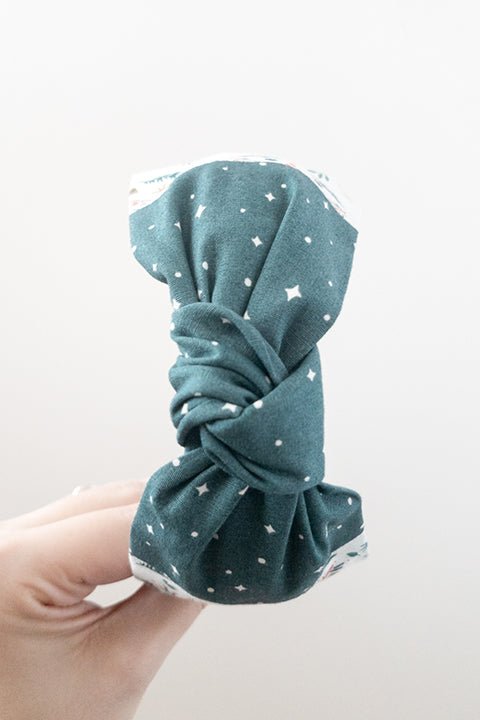top view of an upcycled cotton fabric headband featuring a top knot and color-blocked prints, one with candy canes and gingerbread and the other a green starry night print