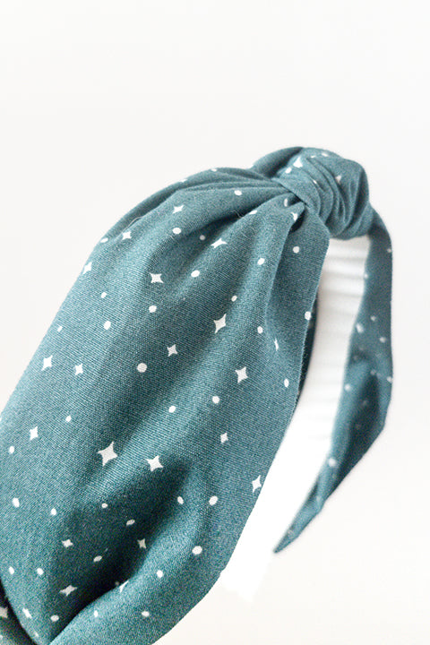 side detail view of an upcycled cotton fabric headband featuring a top knot and forest green holiday starry night print fabric