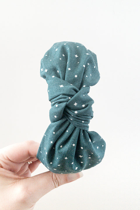 top view of an upcycled cotton fabric headband featuring a top knot and forest green holiday starry night print fabric