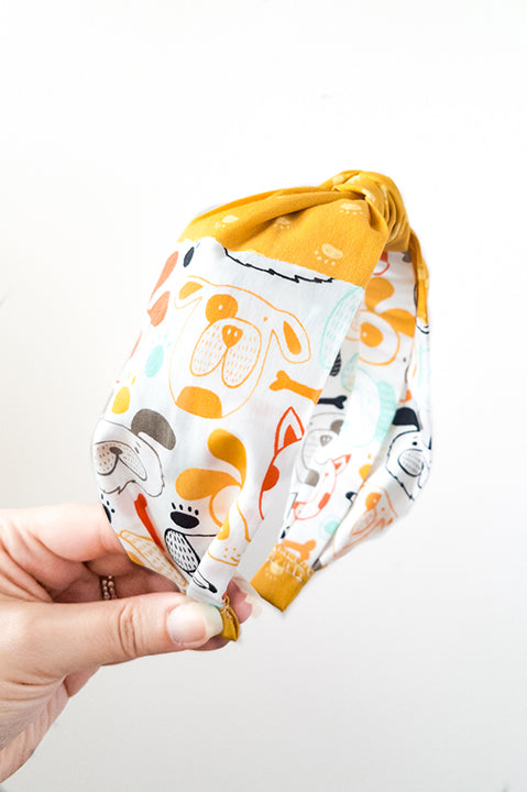 side view of an upcycled cotton fabric headband featuring a top knot and two fabric prints, one featuring mustard yellow paw prints and the other with colorful dog faces