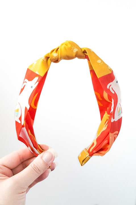 front view of an upcycled handmade headband crafted using two different cotton scrap fabrics, a red print with dogs and puppies and a mustard yellow print with paws