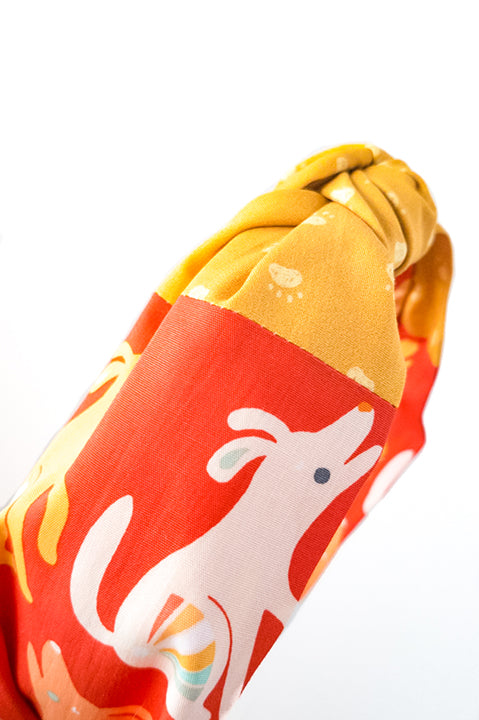 detailed side view of an upcycled handmade headband crafted using two different cotton scrap fabrics, a red print with dogs and puppies and a mustard yellow print with paws