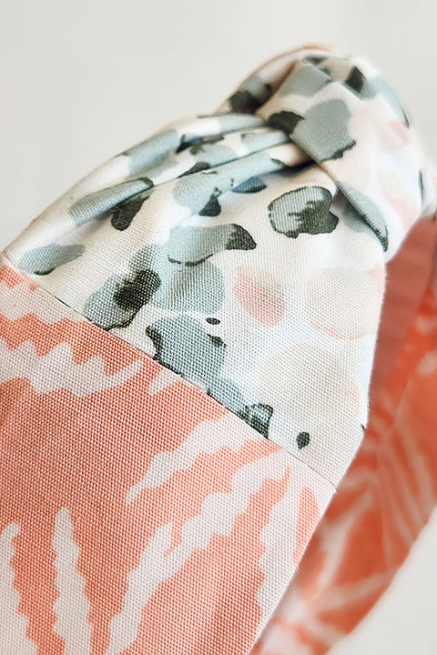 zoomed in detailed view of a two tone top knot style handmade headband. Sustainably made from 100% cotton fabric scraps in two prints, one a pink and sage green watercolor dot floral and the other white ferns on a blush pink background.
