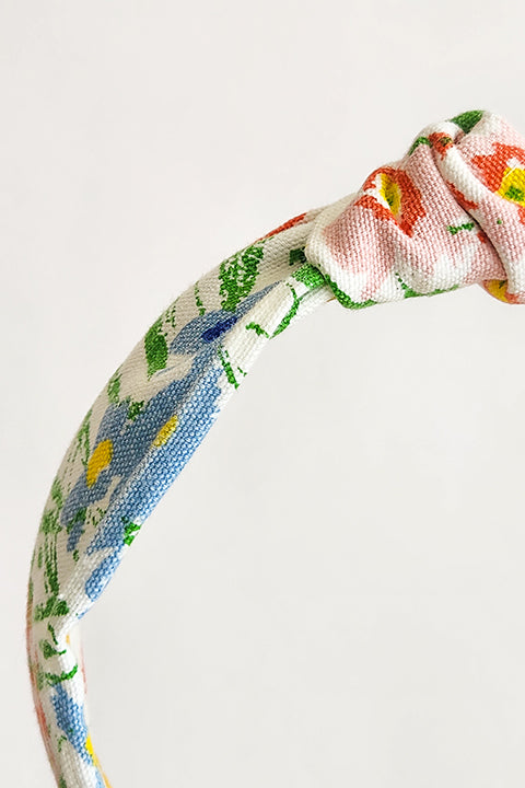 zoomed in detailed image of a handmade top knot style headband in front of a white background. Sustainably made from 100% cotton vintage floral curtains. the floral print is in red, blue, yellow, green and white.