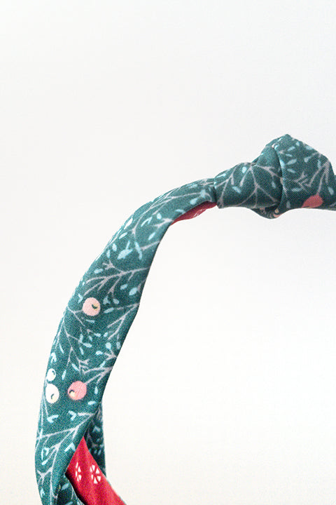 front detail view of an upcycled cotton fabric headband featuring a top knot and a green and red winter berries print fabric