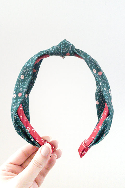 front view of an upcycled cotton fabric headband featuring a top knot and a green and red winter berries print fabric
