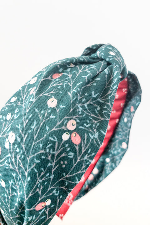 side detail view of an upcycled cotton fabric headband featuring a top knot and a green and red winter berries print fabric