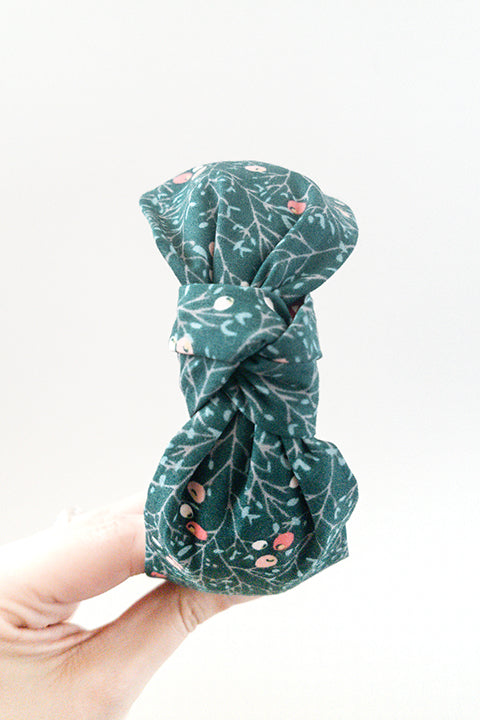 top view of an upcycled cotton fabric headband featuring a top knot and a green and red winter berries print fabric