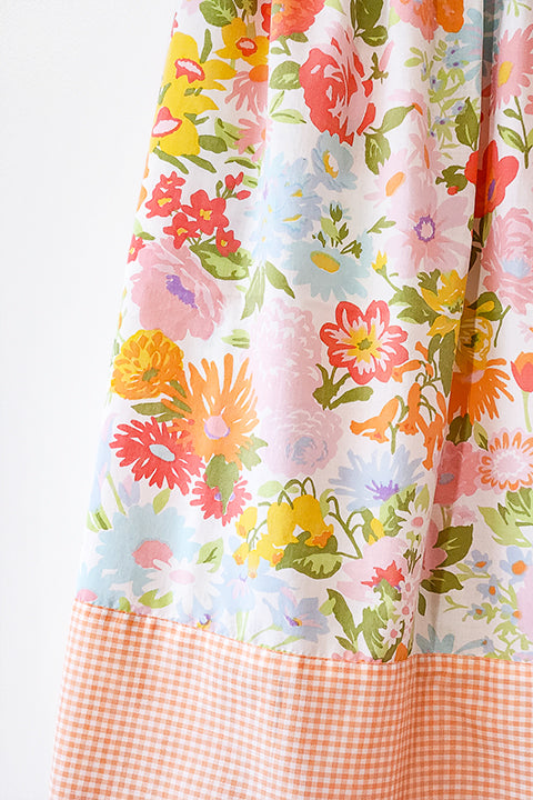 a detailed view of the fabrication of a skirt.  the vintage floral print has a variety of large flowers in pink, orange, yellow, blue and green on a white background.  The second fabric is a small 1/8" gingham check in peach and white.