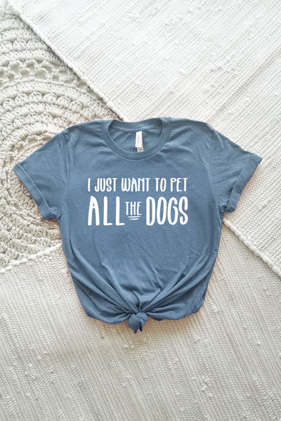 A denim blue adult crewneck triblend tee that says I Just Want to Pet All the Dogs in a white block font.  The t-shirt is laying flat on an off-white textile background and is shown tied with a knot at the hem.