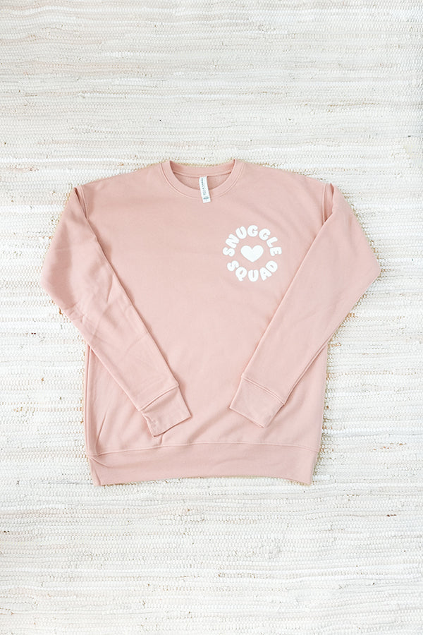 flat lay of Snuggle Squad boxy cut Bella and Canvas sponge fleece sweatshirt in peach pink on a white textile background