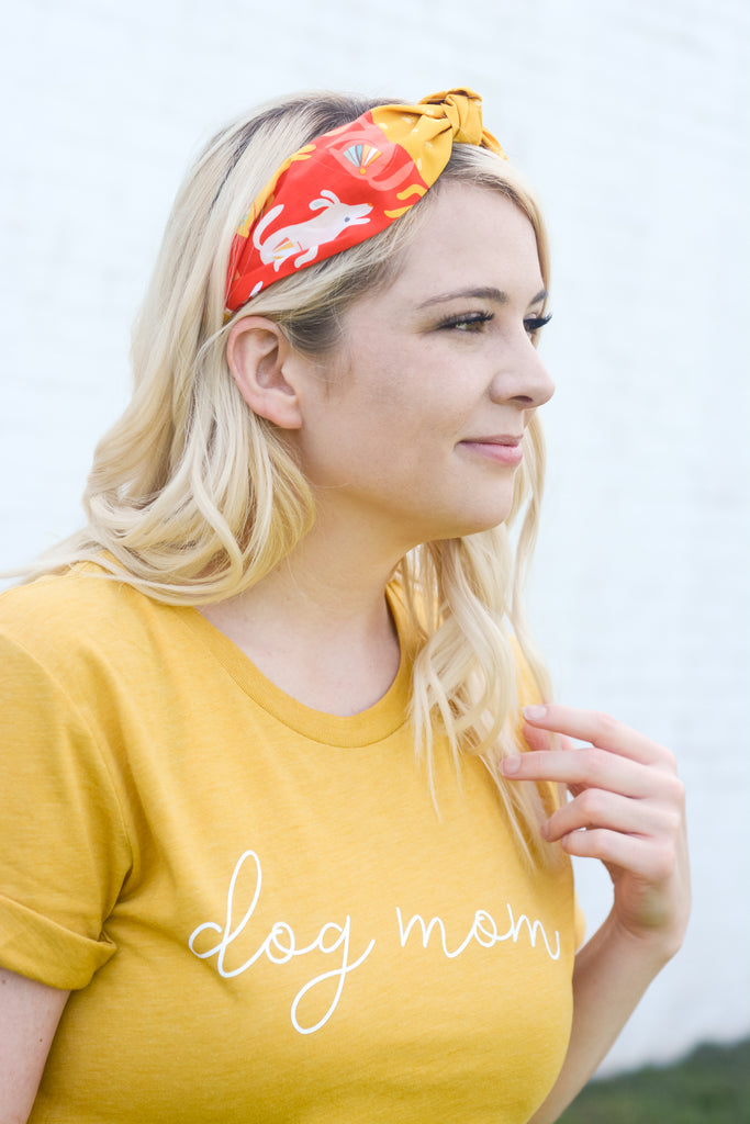blonde female model wearing the poppin pups red and yellow dog print headband and a mustard yellow dog mom tee